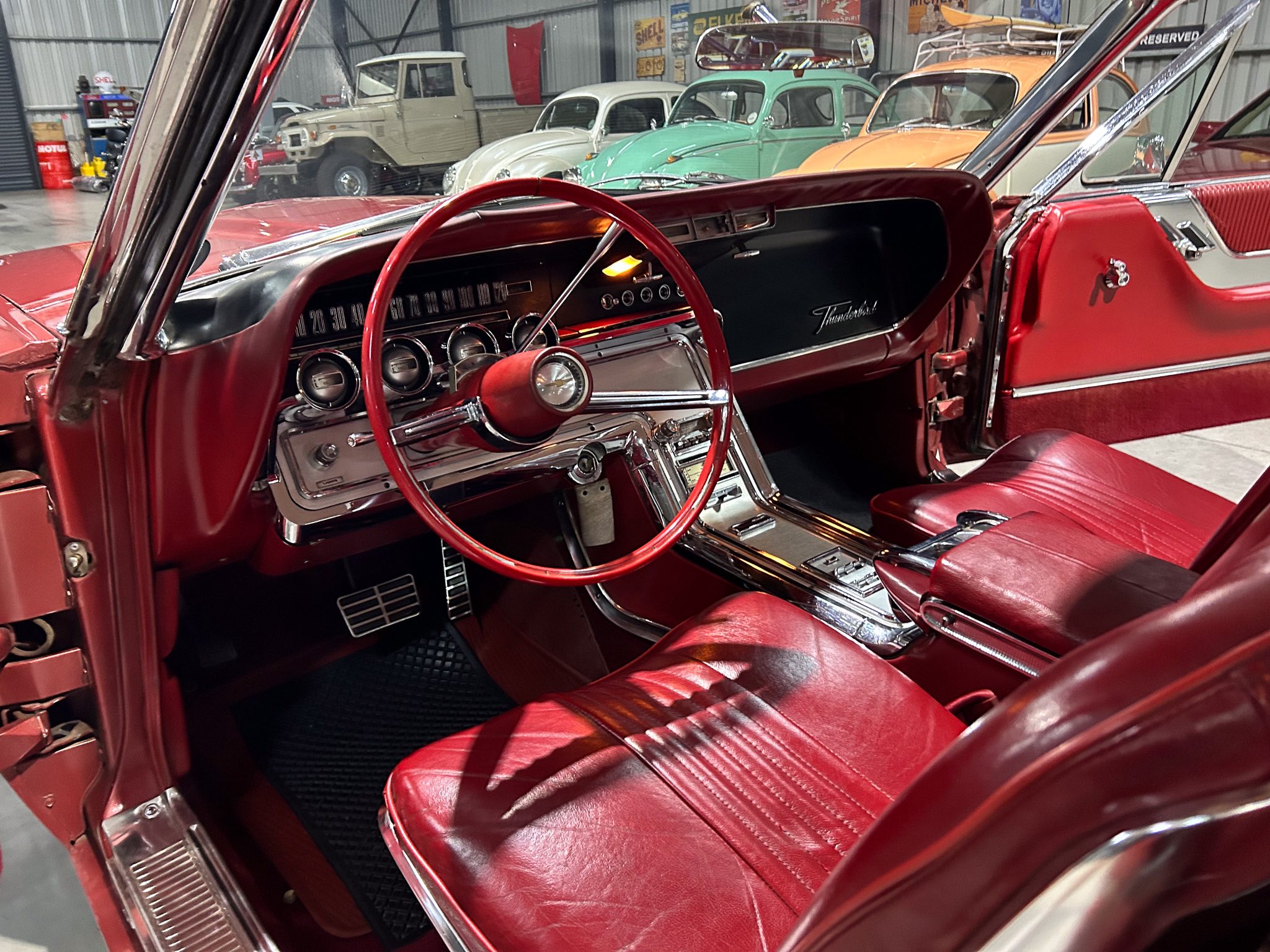 Red vintage car interior with a chrome dashboard, red steering wheel, and red leather seats in a showroom setting.