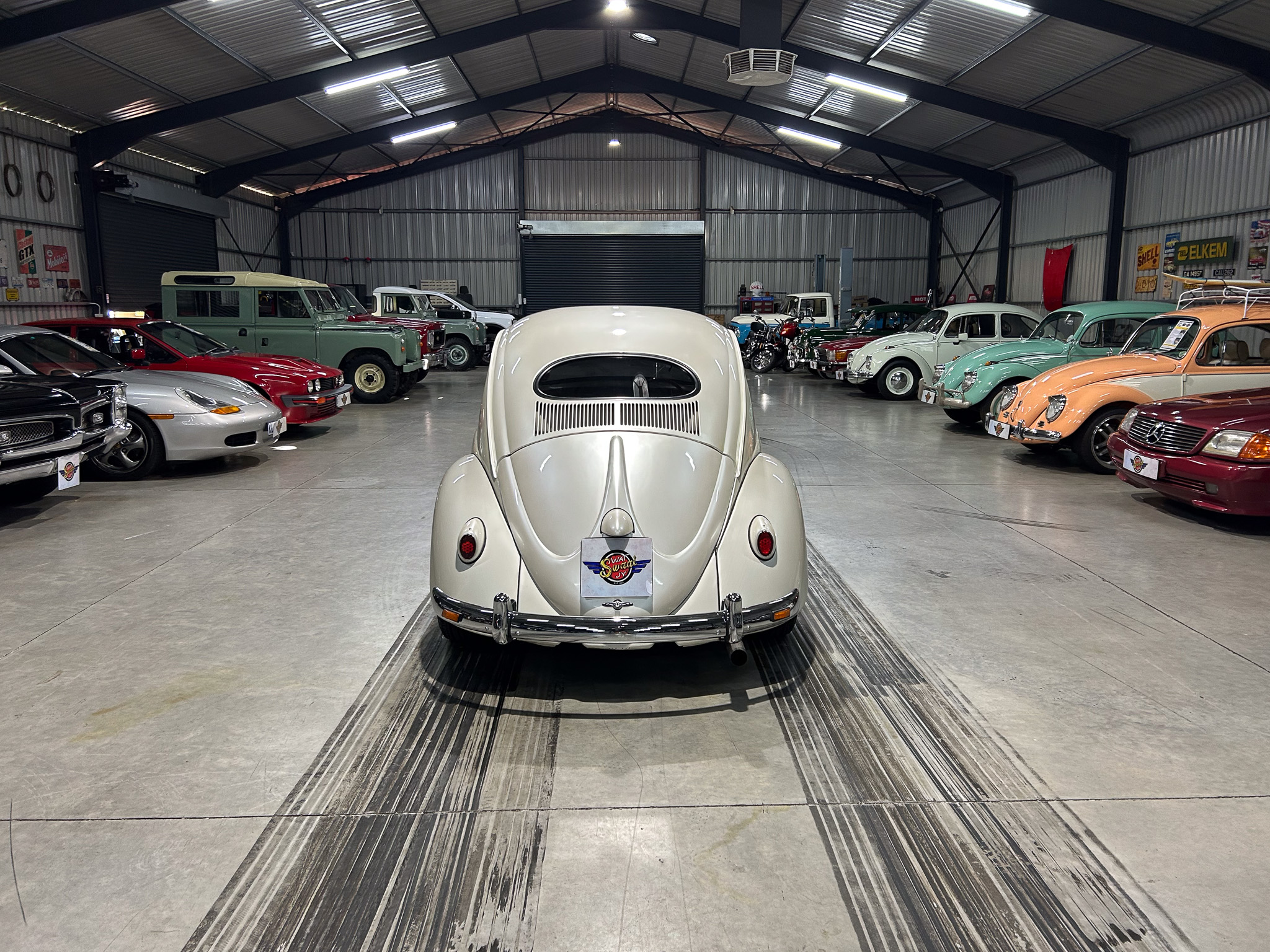 Indoor showroom full of vintage cars, with a white classic car facing the camera in the foreground.