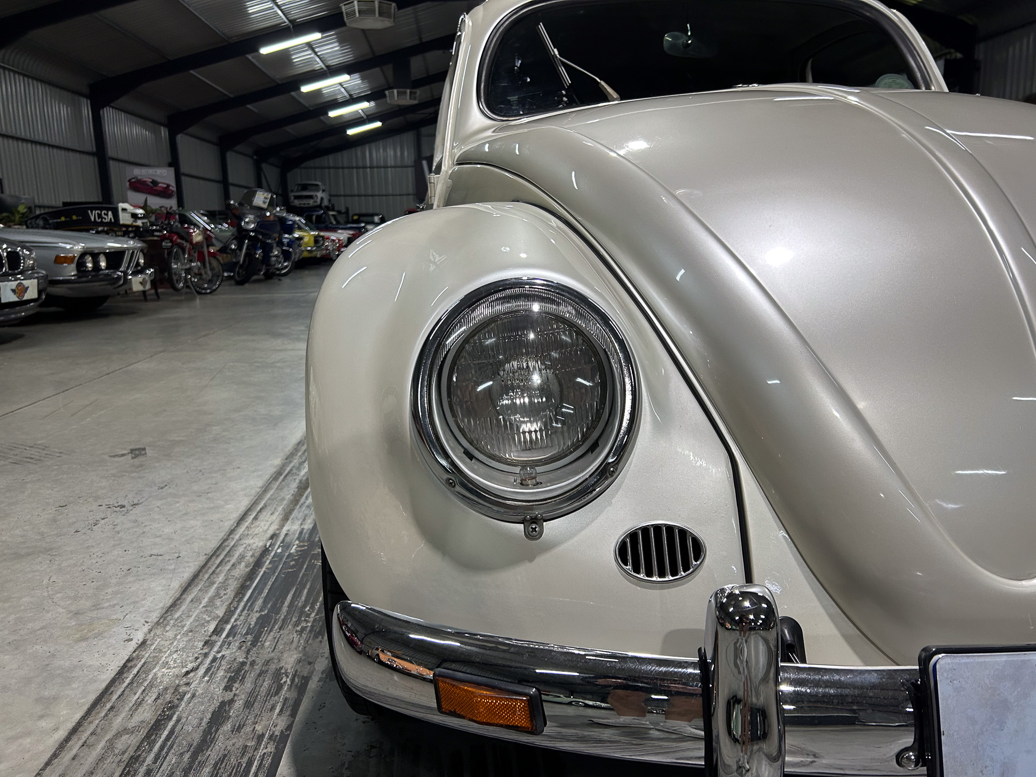 Close-up of a silver vintage car's headlight and curved fender in a showroom with other classic cars in the background.