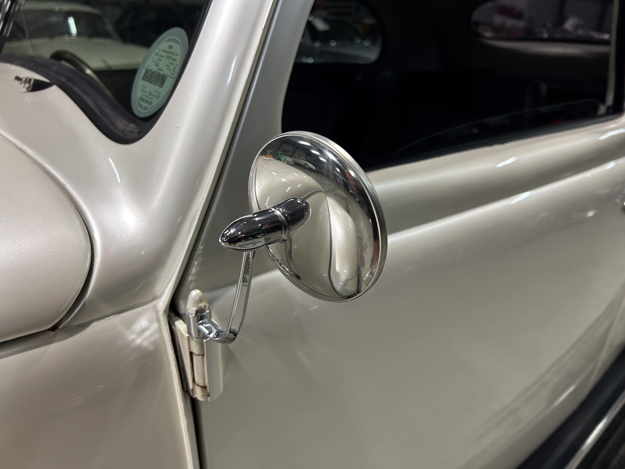 Close-up of a vintage car's front fender with a chrome side mirror and a windshield sticker visible through the window