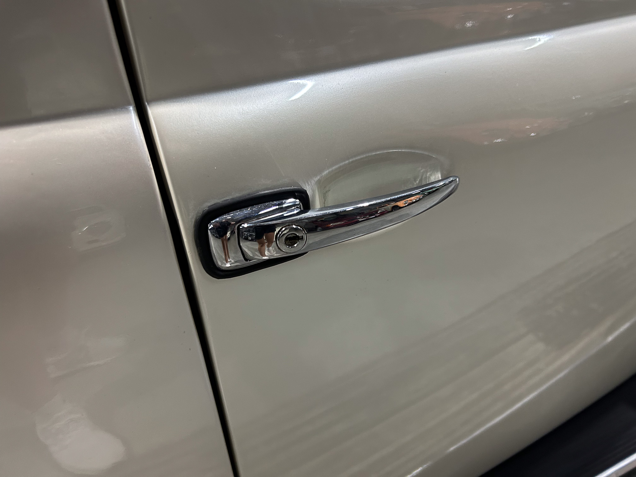 Close-up of a silver car door handle with a small dent and scratch on the panel.
