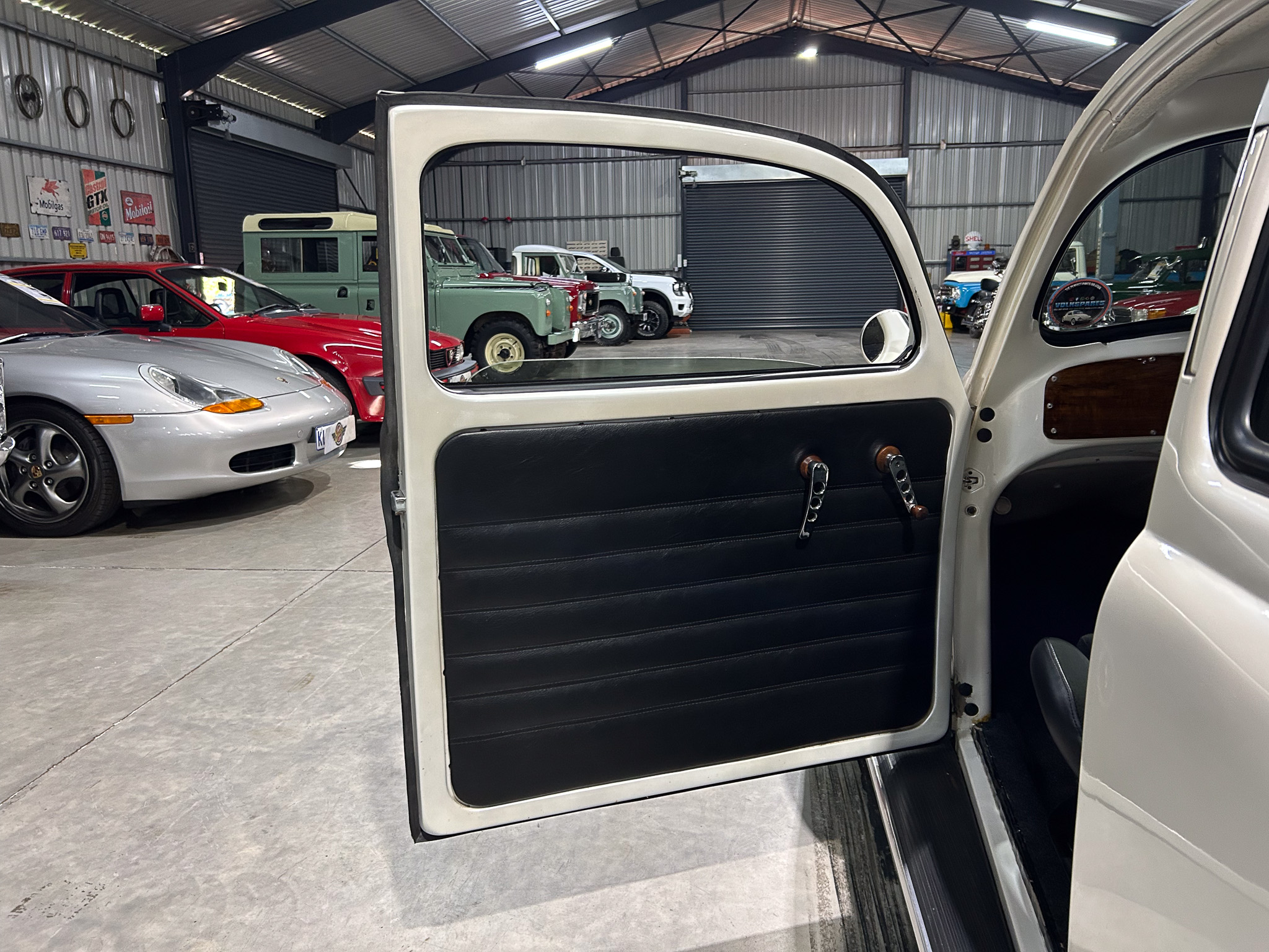 Open car door in foreground of a vintage car showroom, with classic cars lined up inside a metal shed.