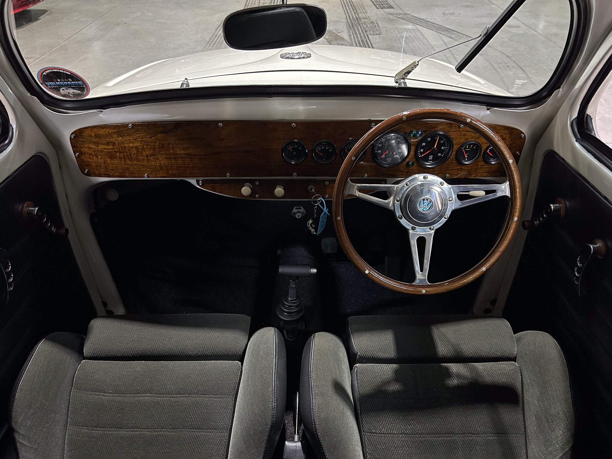 Vintage car interior showing wood dashboard, analog gauges, and a wooden steering wheel with metal spokes viewed from the driver seat.