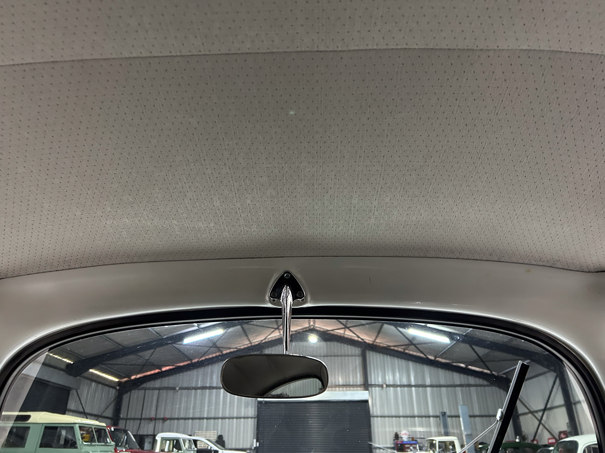 Interior view of a car's front cabin showing a perforated headliner, rearview mirror, and windshield in a showroom setting.