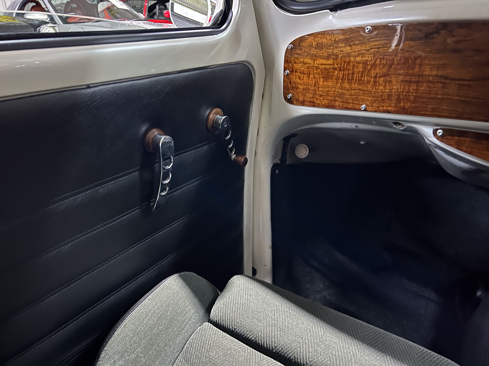 Interior of a vintage car door: dark padded panel, manual window crank, and wood-grain trim with chrome hardware.