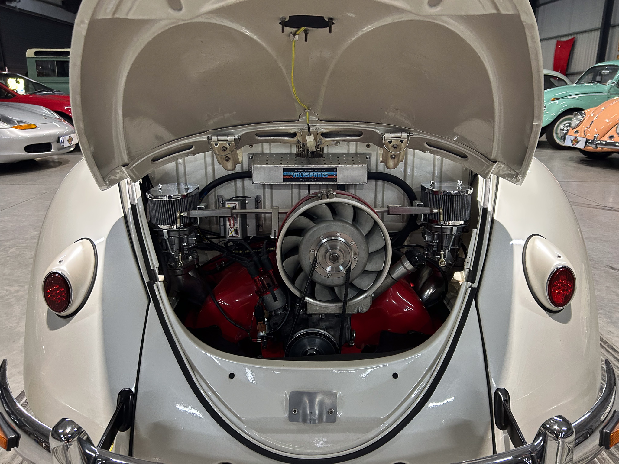 Open rear engine bay of a classic Porsche 356 showing the air-cooled engine and mechanical components in a showroom setting.