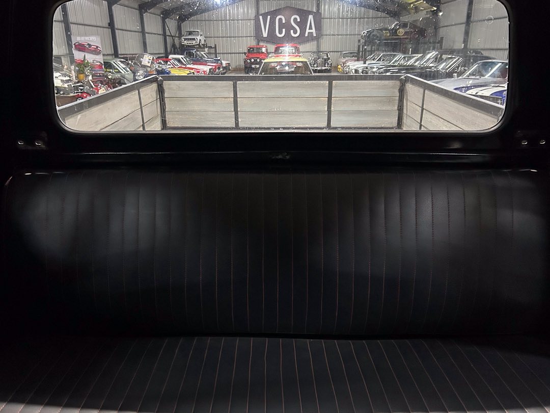 Backseat of a vintage car with black vertical-striped upholstery, looking out the rear window at a car showroom with a large VCSA sign.