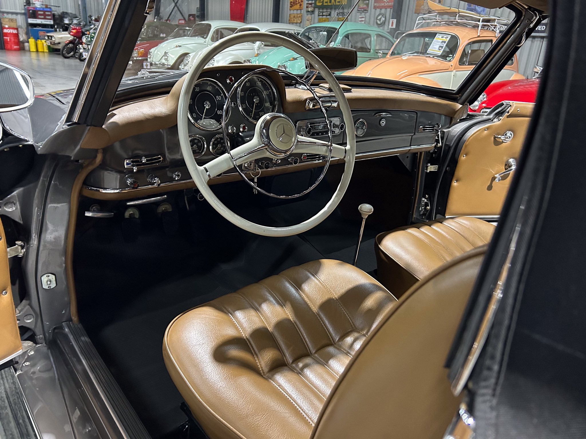 Interior of a classic car showcasing a tan leather dashboard and large white steering wheel with chrome trim