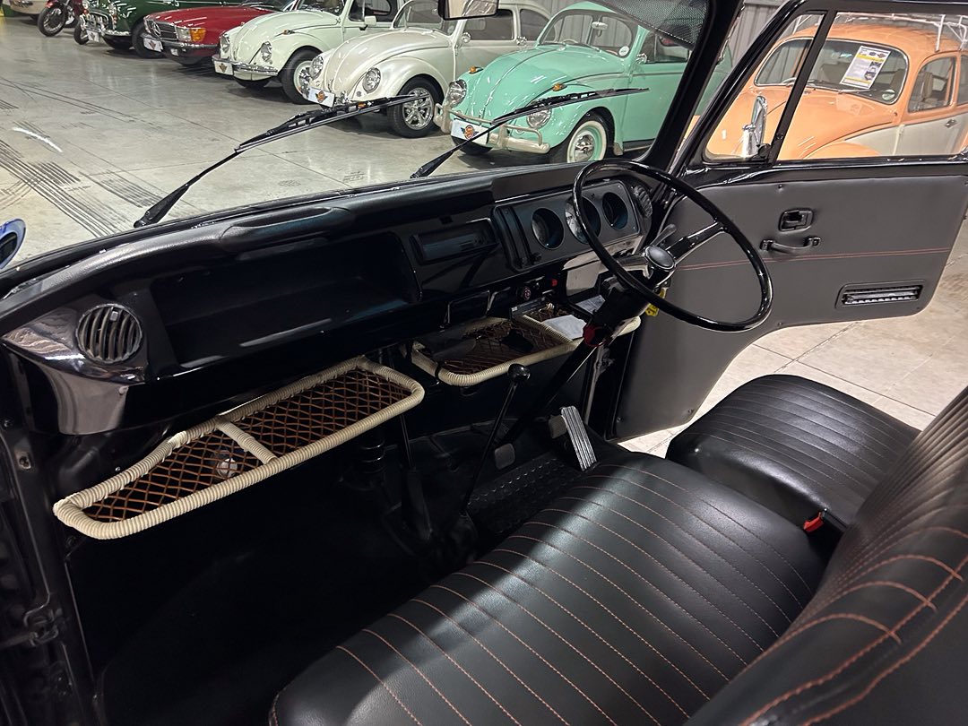 Interior of a vintage car with black leather seats and a large steering wheel; classic dashboard and door open in a showroom setting.