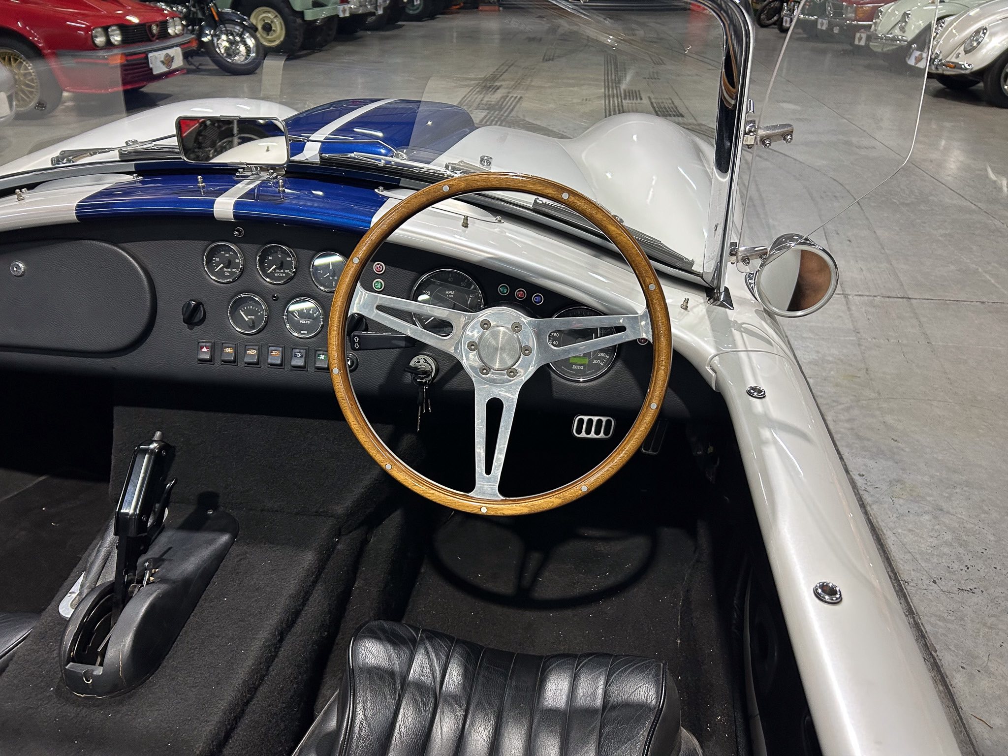 Classic car interior: wooden steering wheel, analog gauges, and black leather seats, viewed from the driver's side.
