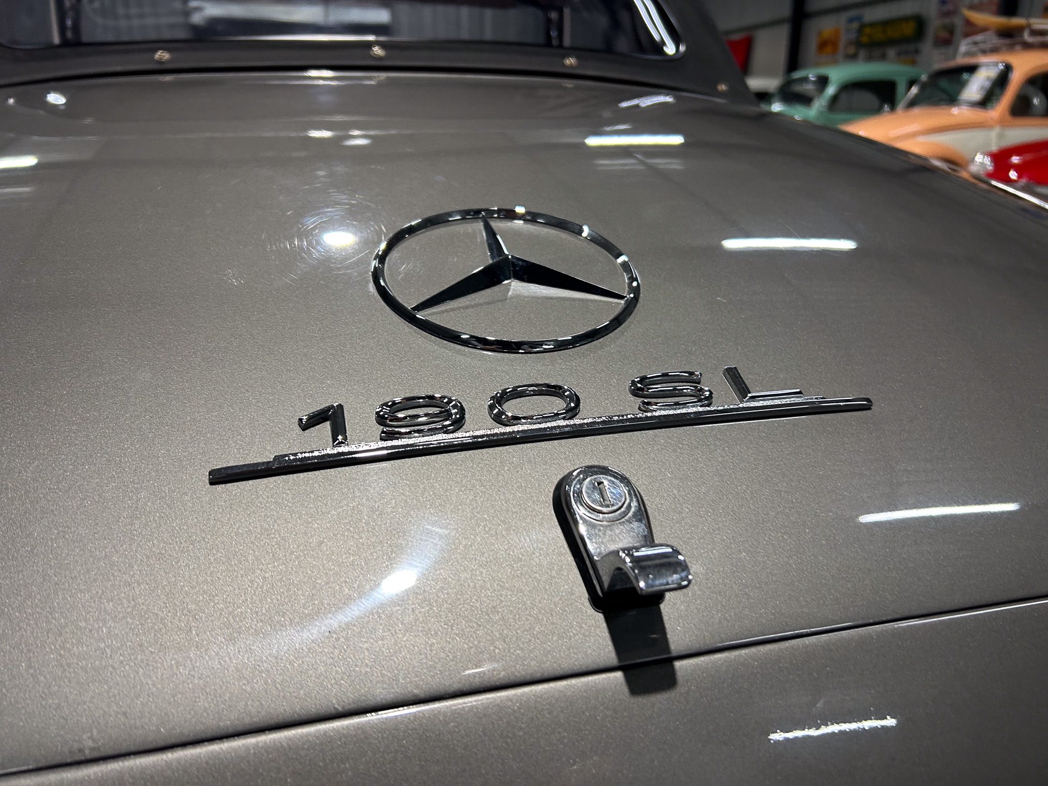 Close-up of a Mercedes-Benz hood emblem centered on a metallic gray car hood in a showroom.