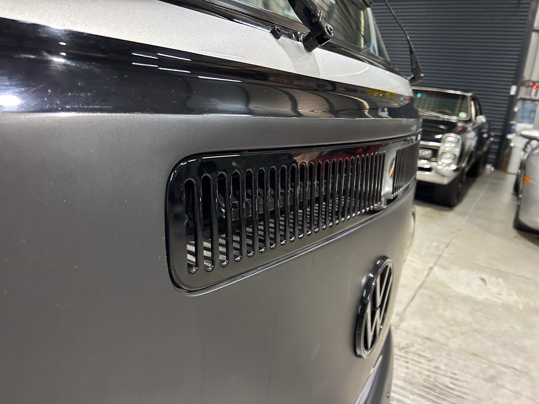 Front view of a gray Volkswagen van with a black vent grille and VW emblem, parked in a showroom or garage.