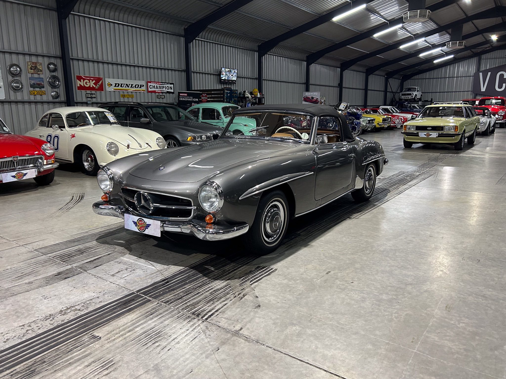 Indoor car museum with vintage cars lined up, including a gray convertible in the foreground.