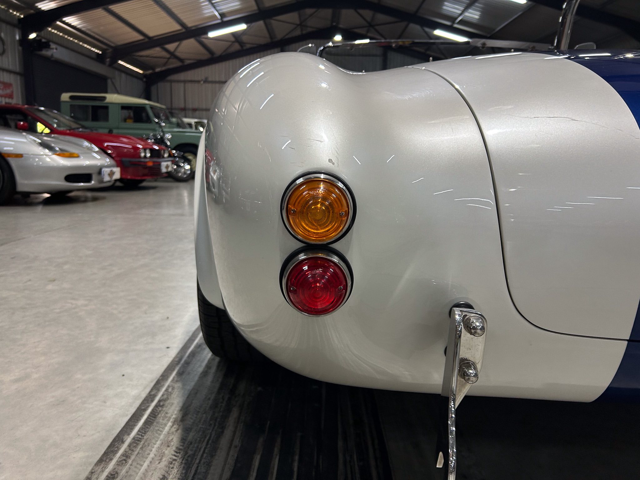 Rear end of a silver classic car with round amber and red taillights in an indoor showroom.