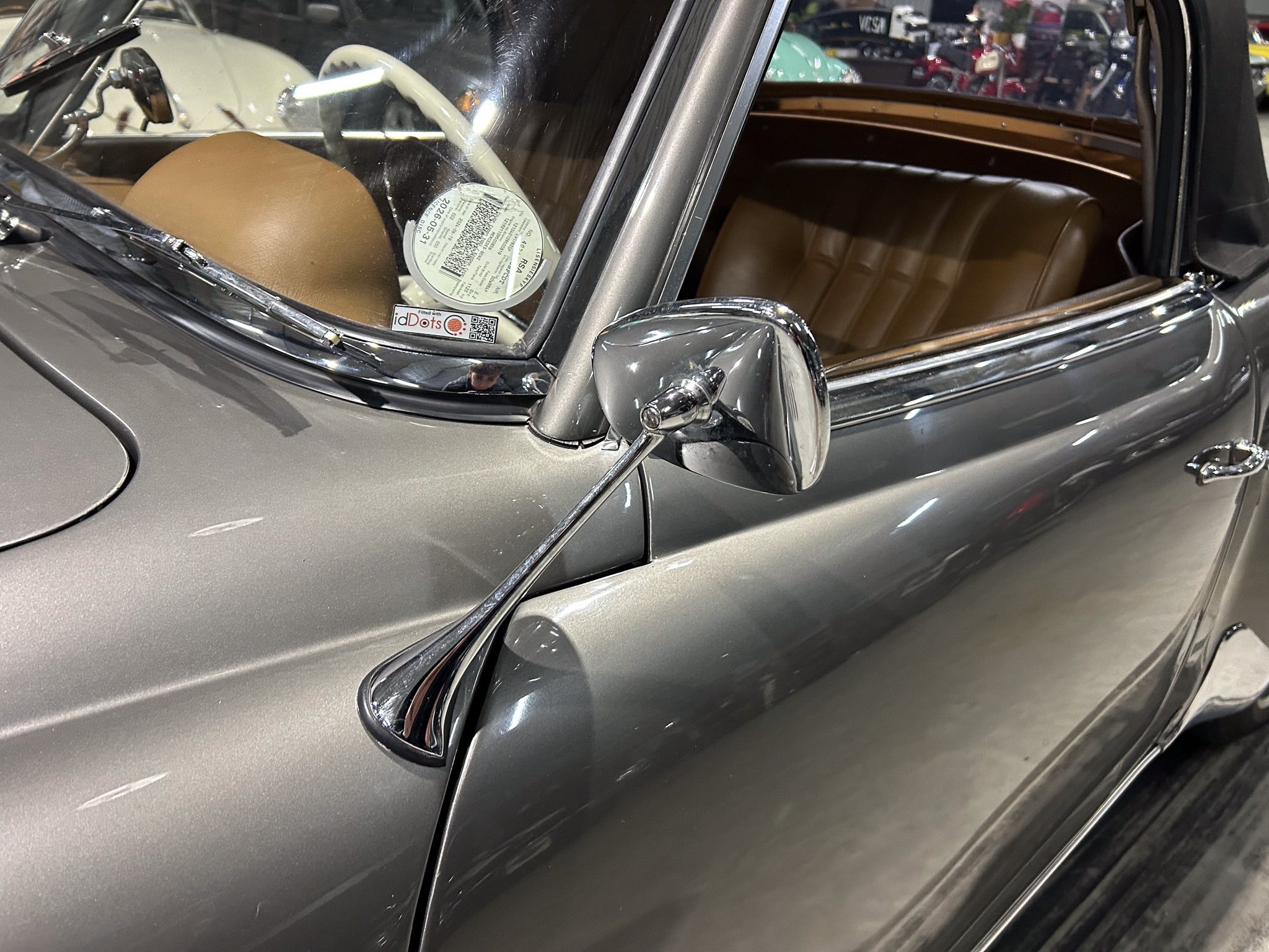 Close-up of a vintage car interior with tan leather seats, chrome trim, and a circular sticker on the windshield window.