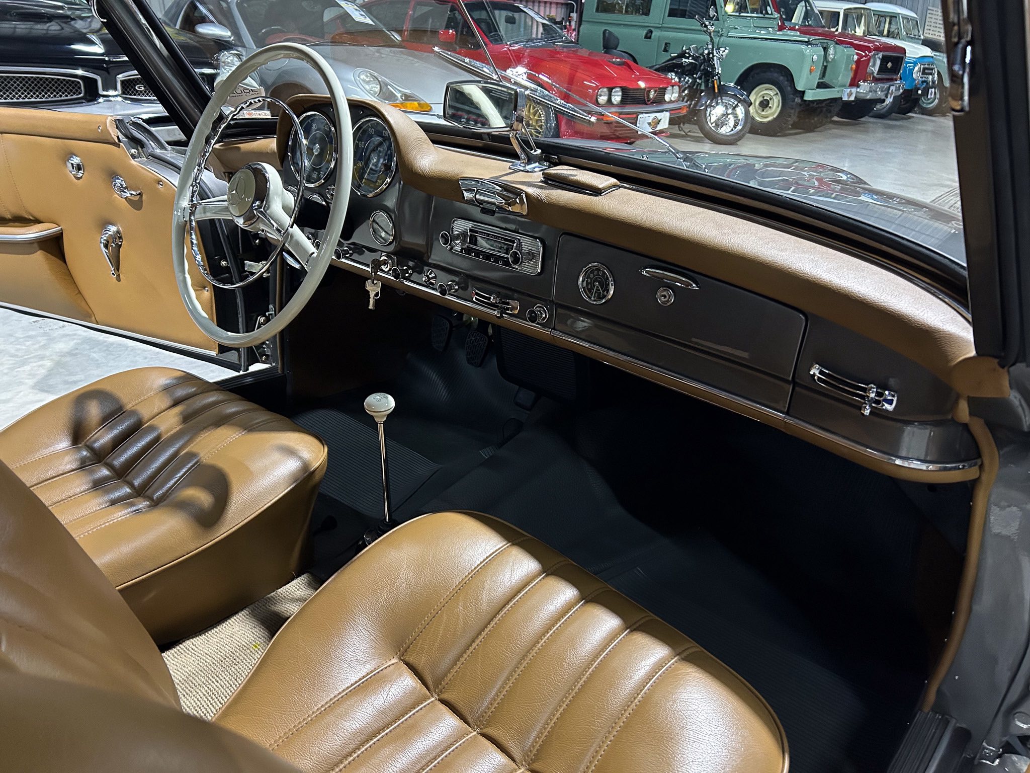 Vintage car interior with tan leather seats and dashboard, chrome accents, and a light-gray steering wheel seen from the passenger side.