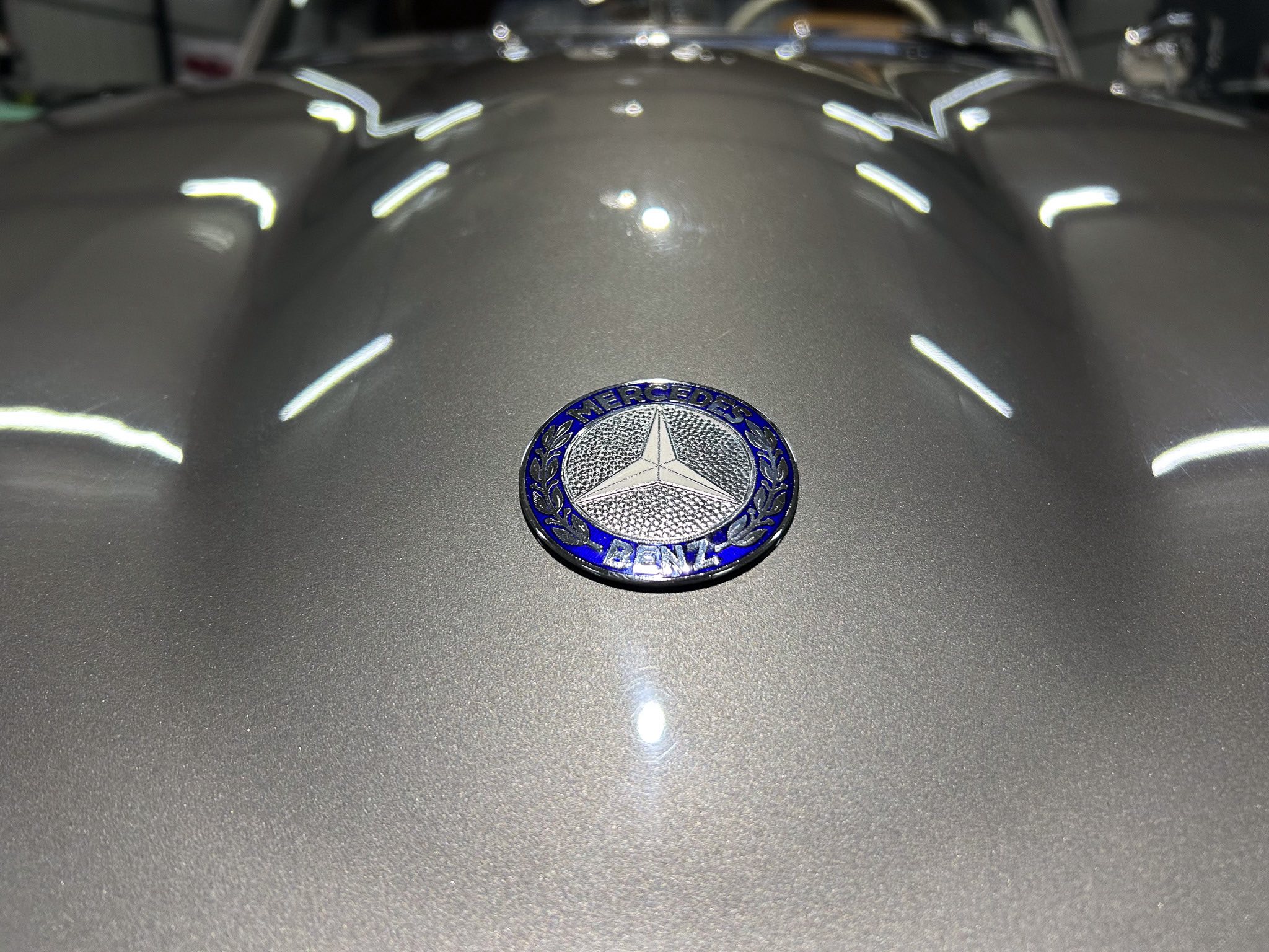Close-up of a Mercedes-Benz emblem centered on a metallic car hood.
