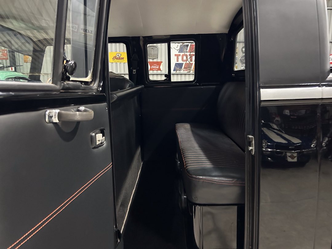Interior of a vintage black van with a single bench seat and red stitching, door open to show the cabin area.