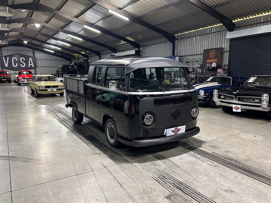Black vintage VW Type 2 van parked in a classic car showroom with other restored vehicles around it.