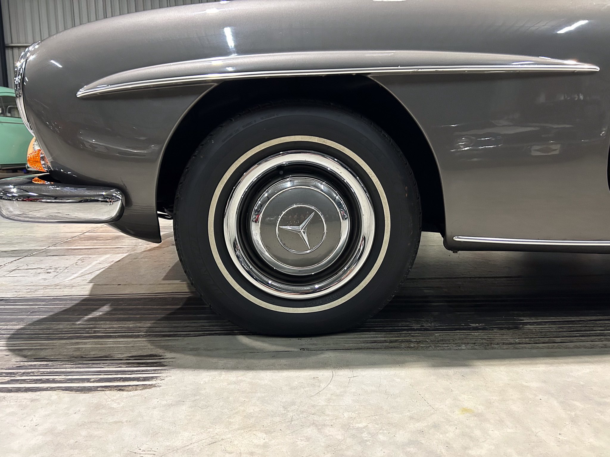 Close-up of a vintage car's front fender, wheel, and chrome trim with a gray body and whitewall tire hubcap featuring a star emblem