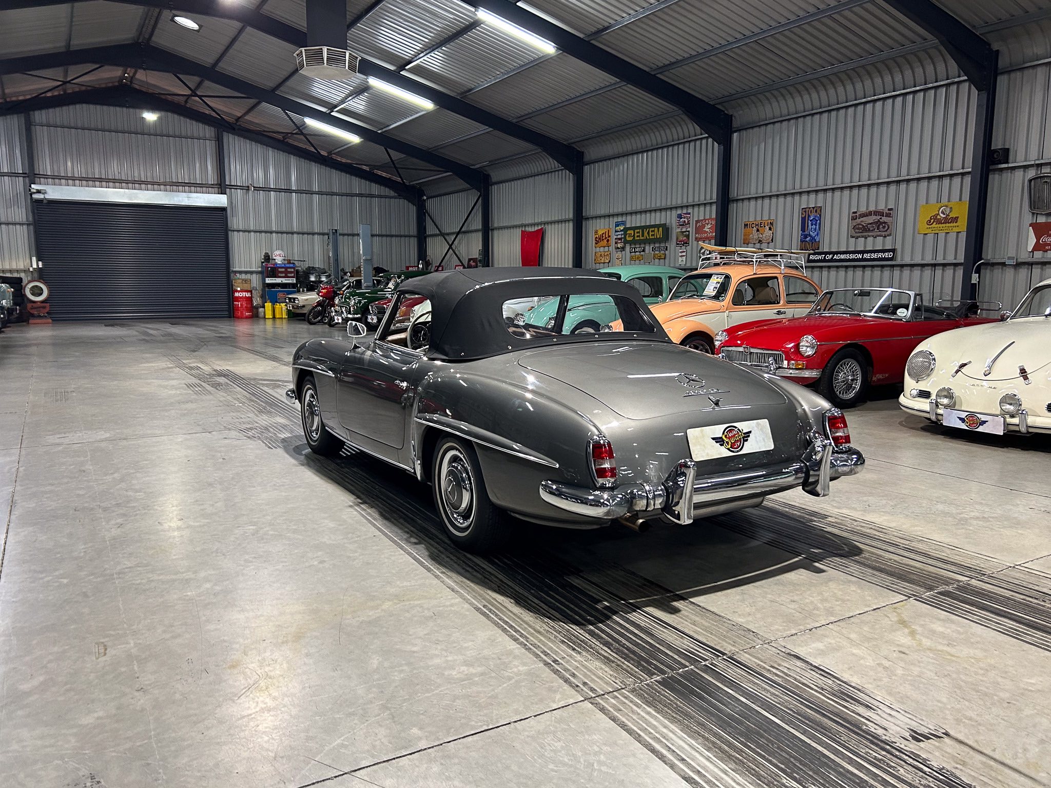 Indoor showroom with a row of vintage convertibles and classic cars on a concrete floor.