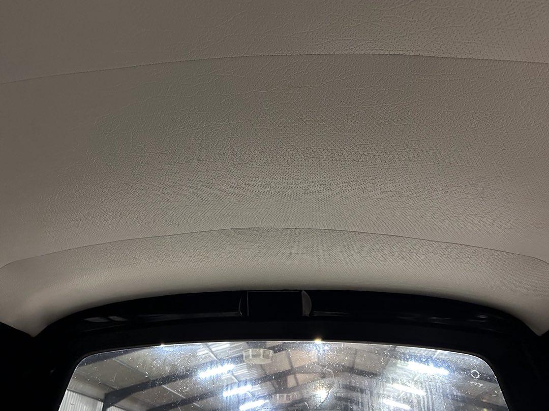 Light gray fabric headliner of a car viewed from the rear seat, with a rear window showing a bright workshop outside.