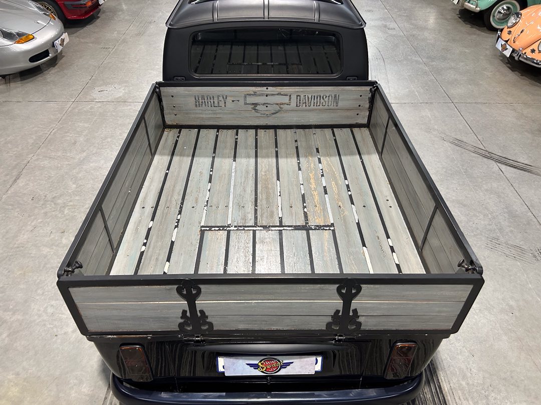 Weathered pickup bed with wooden slats and a faded Harley‑Davidson panel at the cab end, seen from above in a showroom.