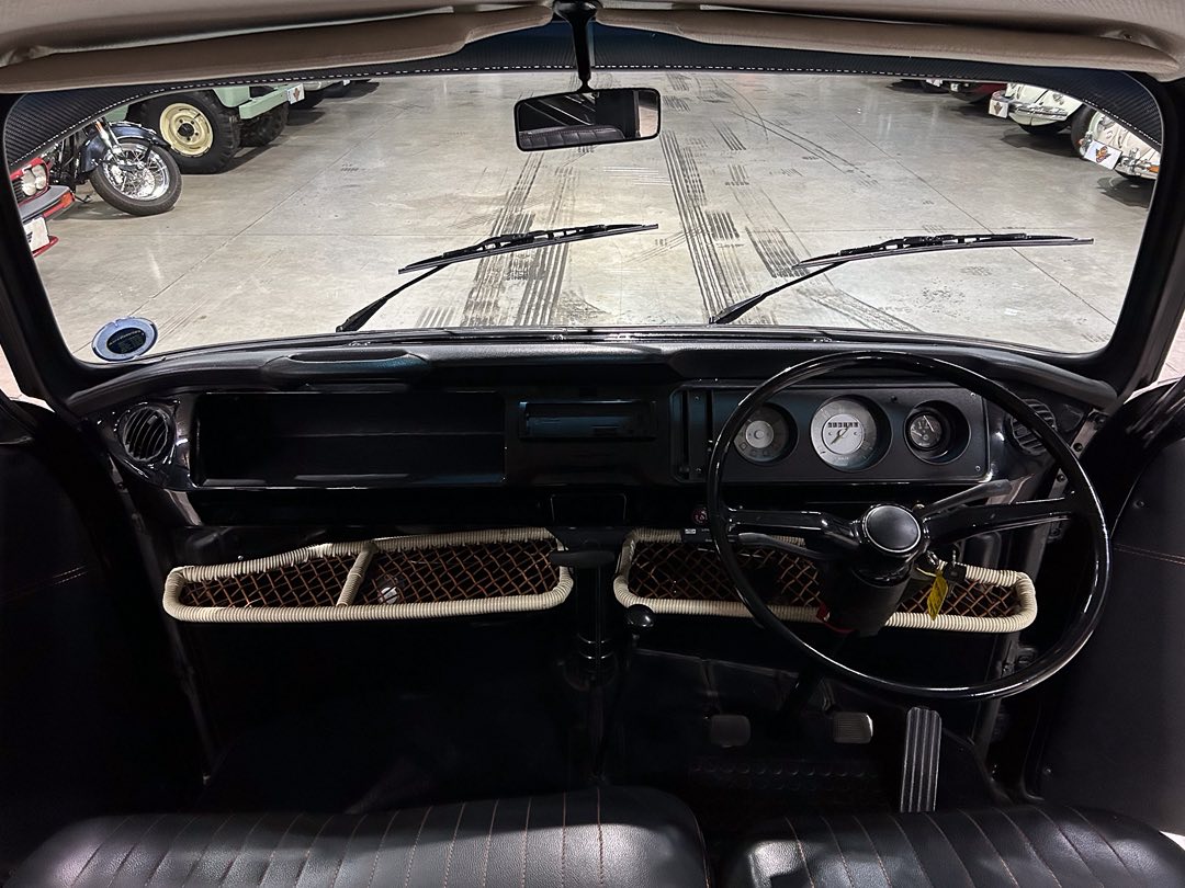 Driver’s view of a vintage car interior with a large steering wheel, round gauges, and woven under-dash storage nets.