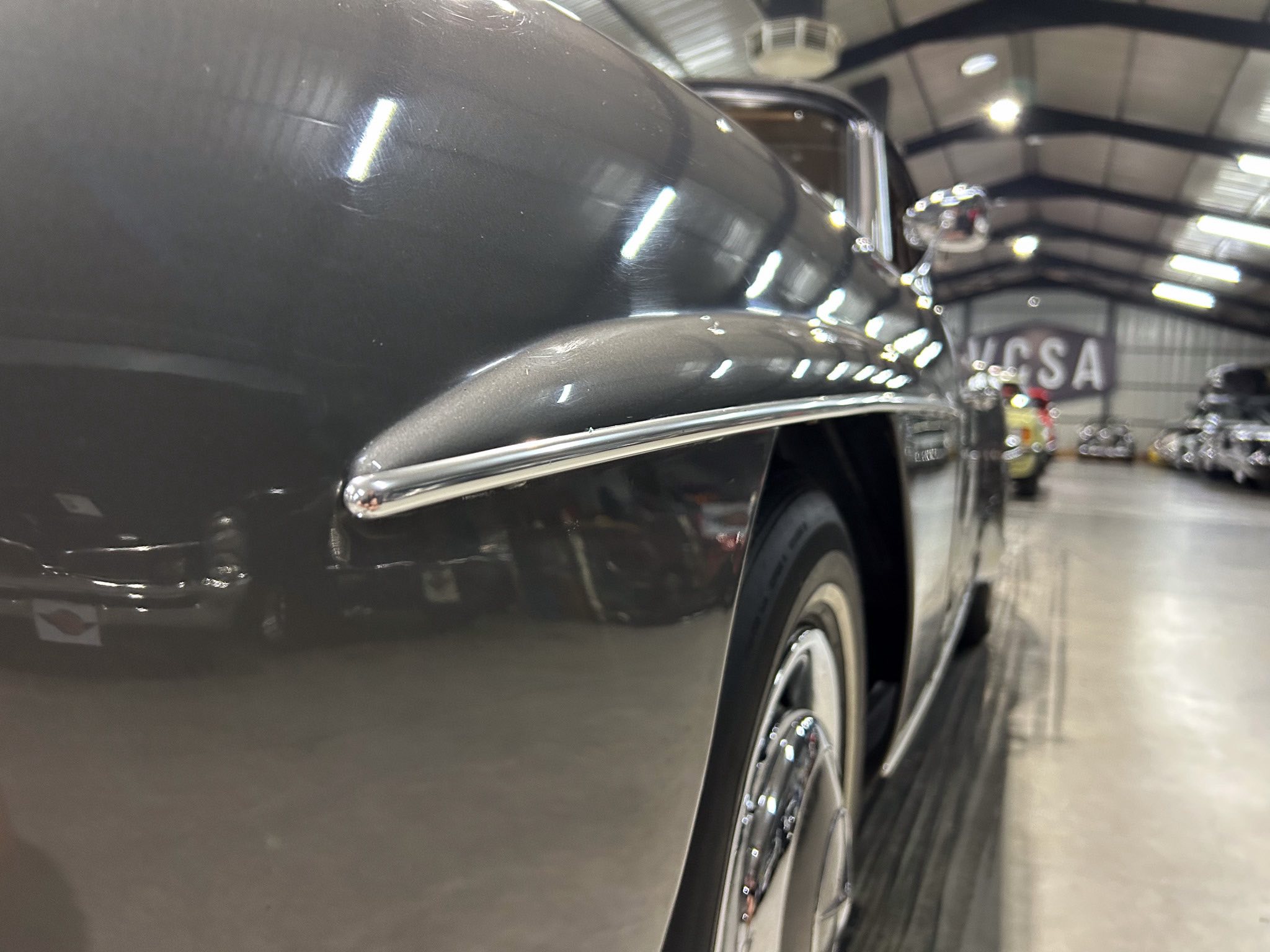 Close-up of a dark car body with chrome trim in an indoor showroom.