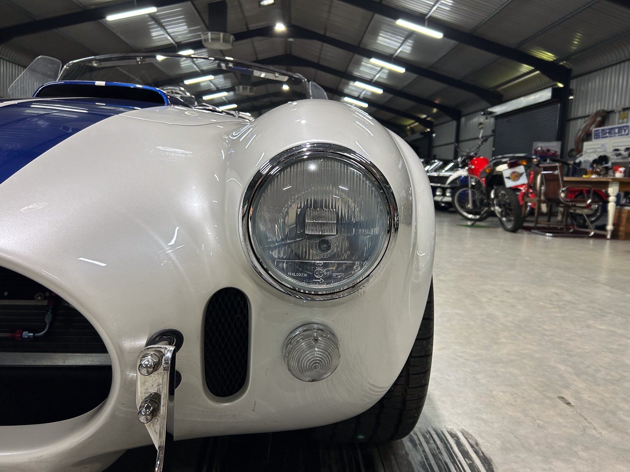 Close-up of a vintage silver car's round headlight and front bumper in a showroom.