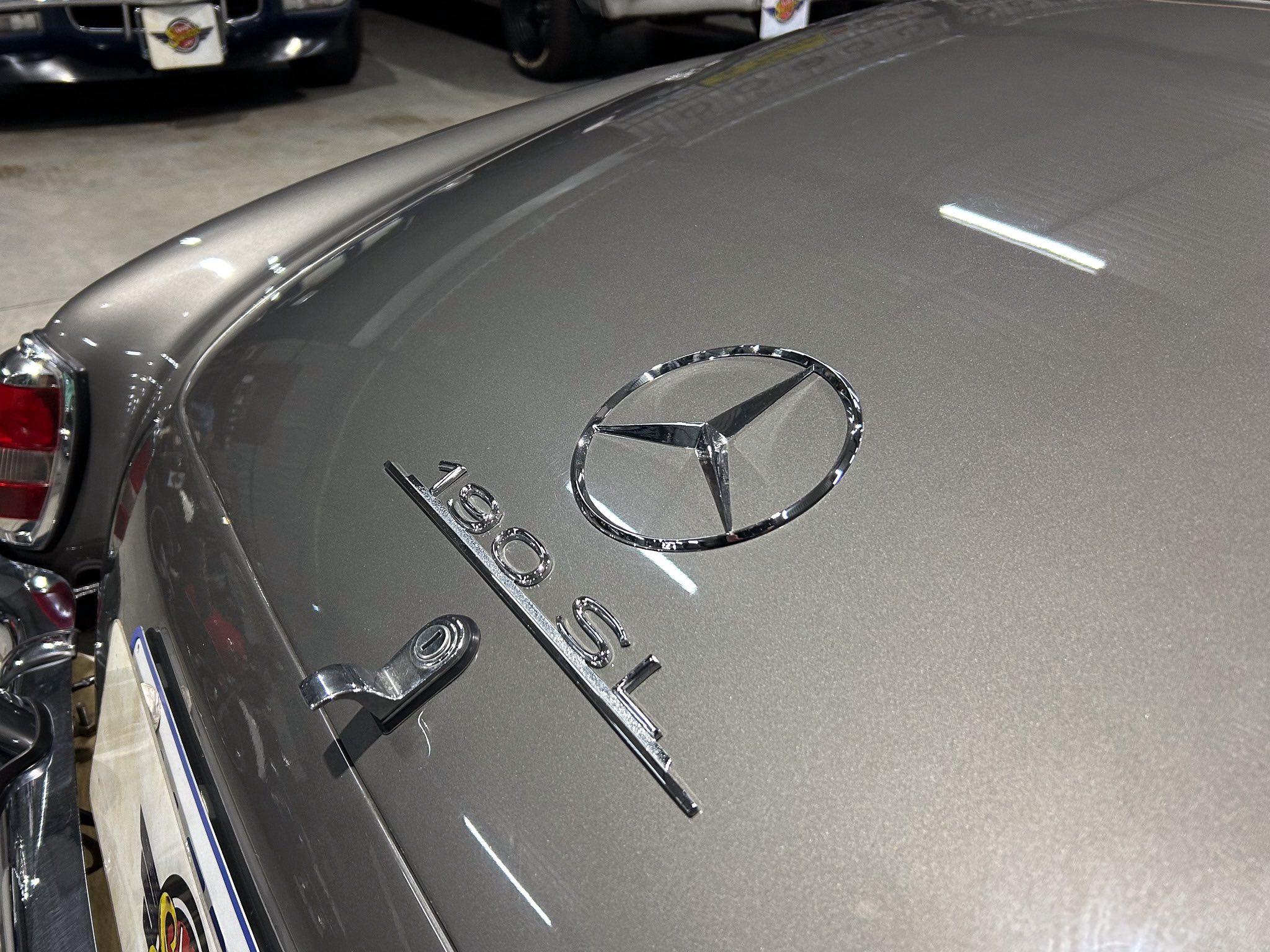 Close-up of a gray Mercedes-Benz hood with a chrome emblem in a car showroom.