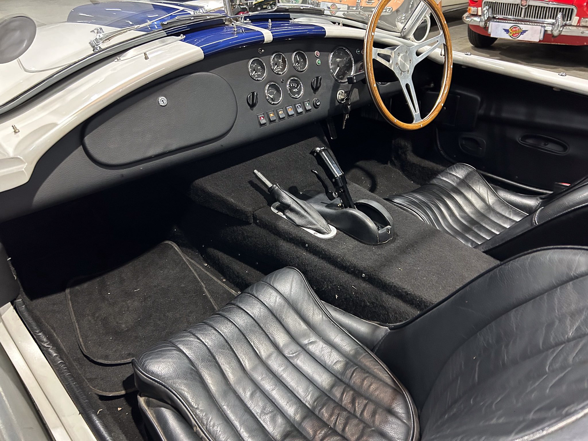 Classic vintage car interior with a wooden steering wheel, gray dash, and multiple round gauges on black upholstery