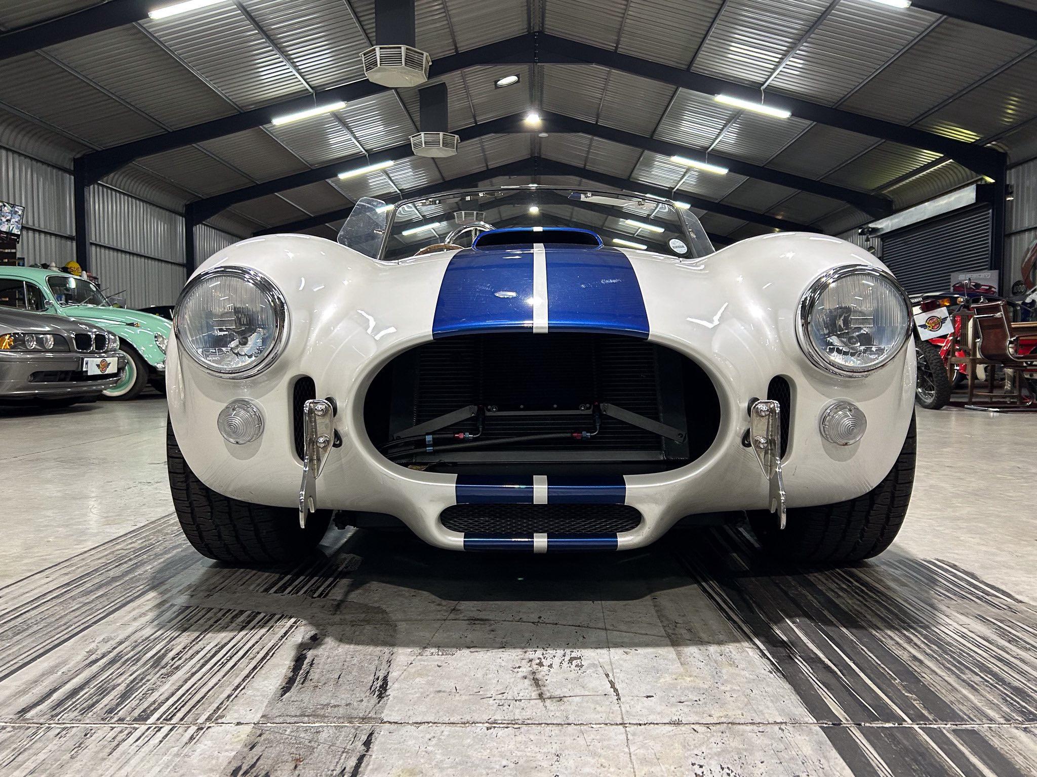Front view of a white vintage race car with a blue center stripe in a showroom.