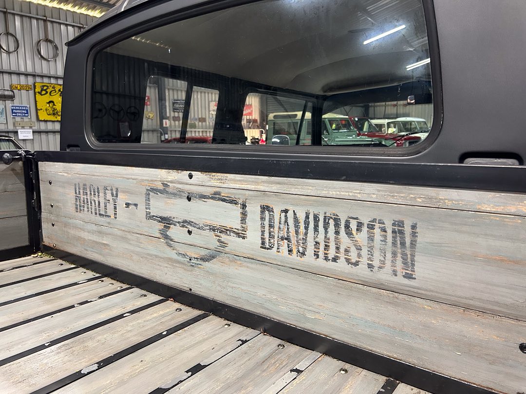 Weathered wooden truck bed side with faded 'DAVIDSON' logo, vintage pickup in a workshop setting.