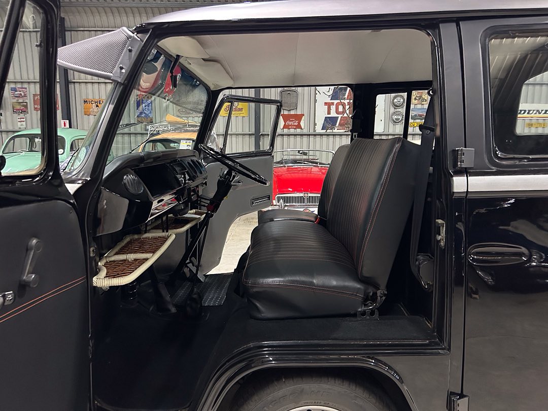 Interior of a vintage black SUV with a front bench seat, exposed pedals, and a classic dashboard visible through the open driver's door