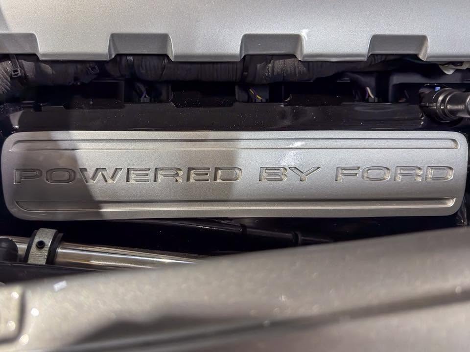 Close-up of a silver engine cover that reads 'POWERED BY FORD' under the hood of a vehicle.