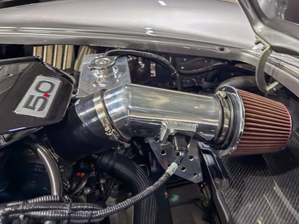 Aftermarket car air intake with a shiny metal pipe and red cone air filter mounted in a vehicle engine bay.
