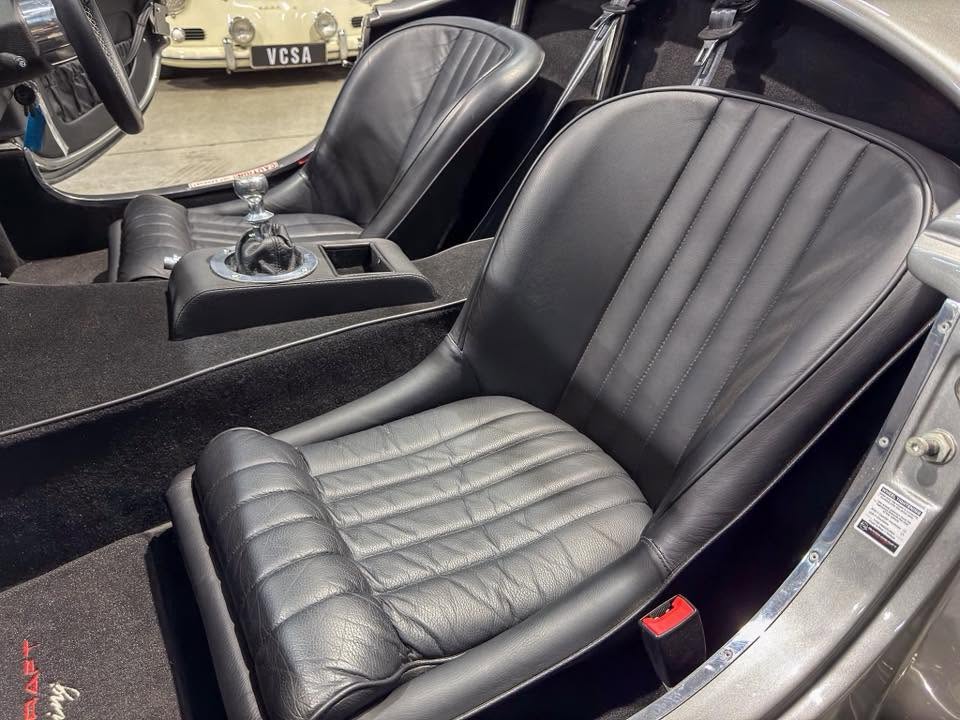 Inside a classic black leather sports car: two bucket seats, center console with manual gear shifter.