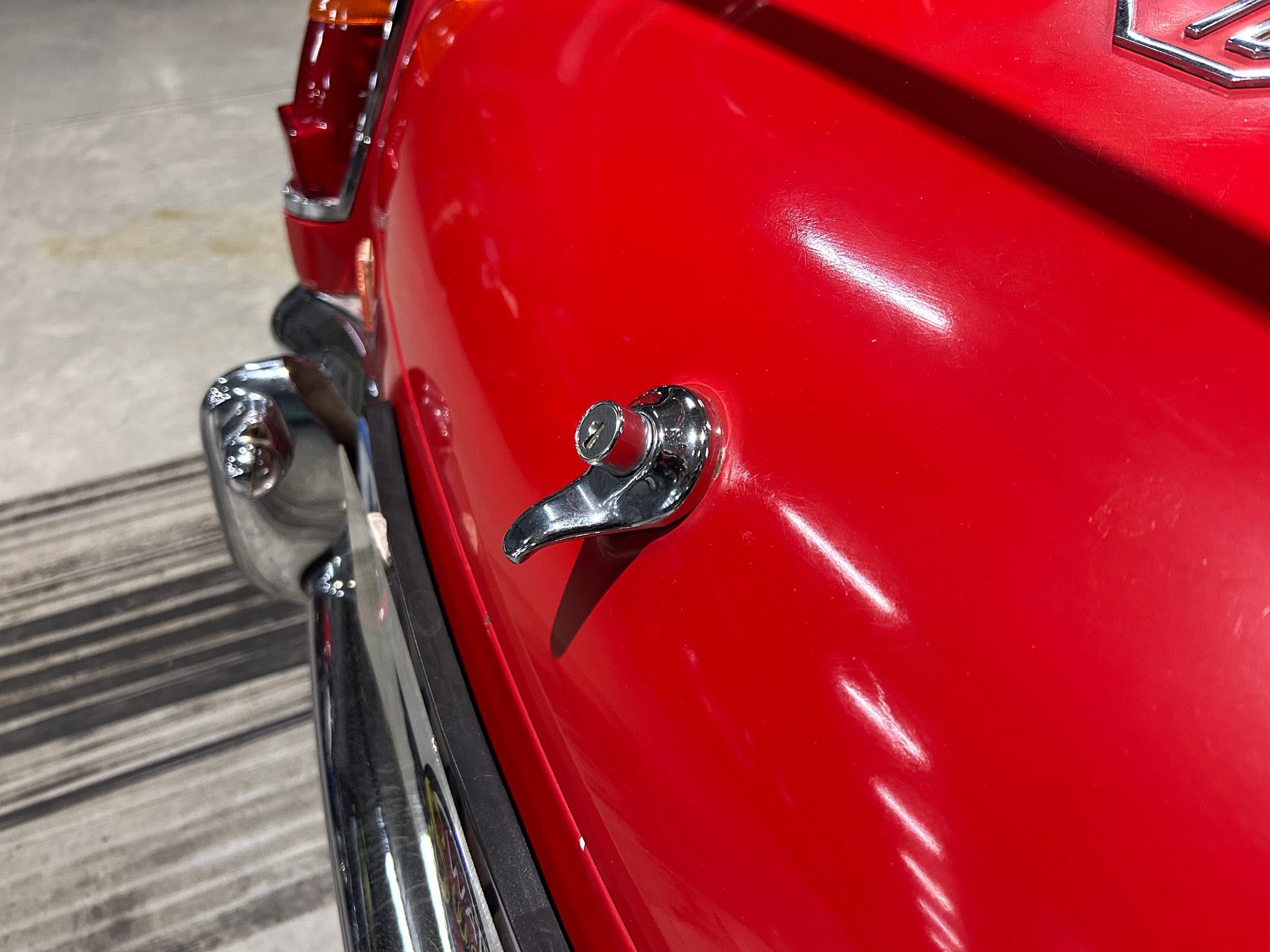 Close-up of a red car's chrome door handle and glossy body panel.