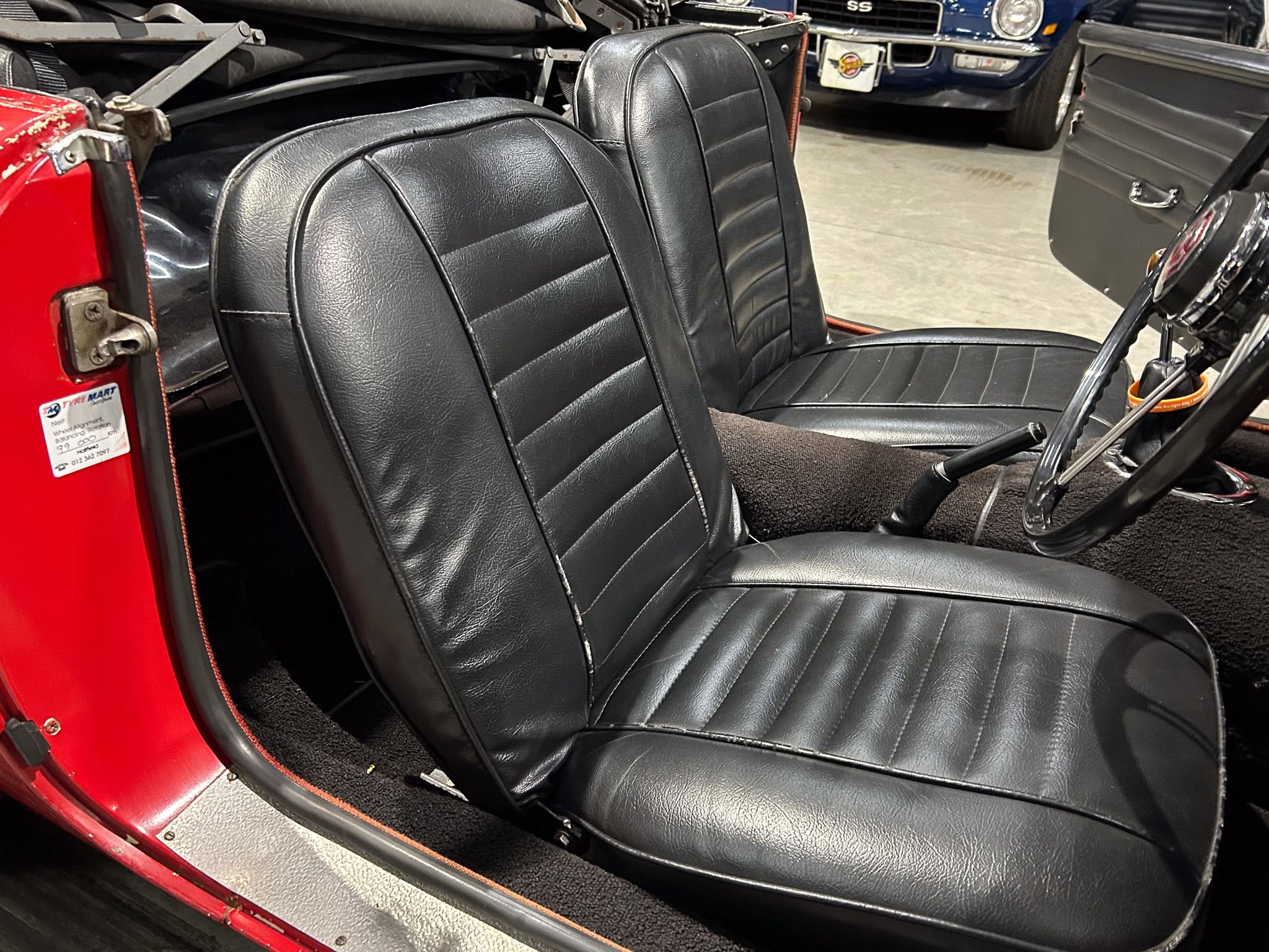 Close-up interior view of a vintage red car, showing black leather bucket seats and part of the chrome steering wheel.