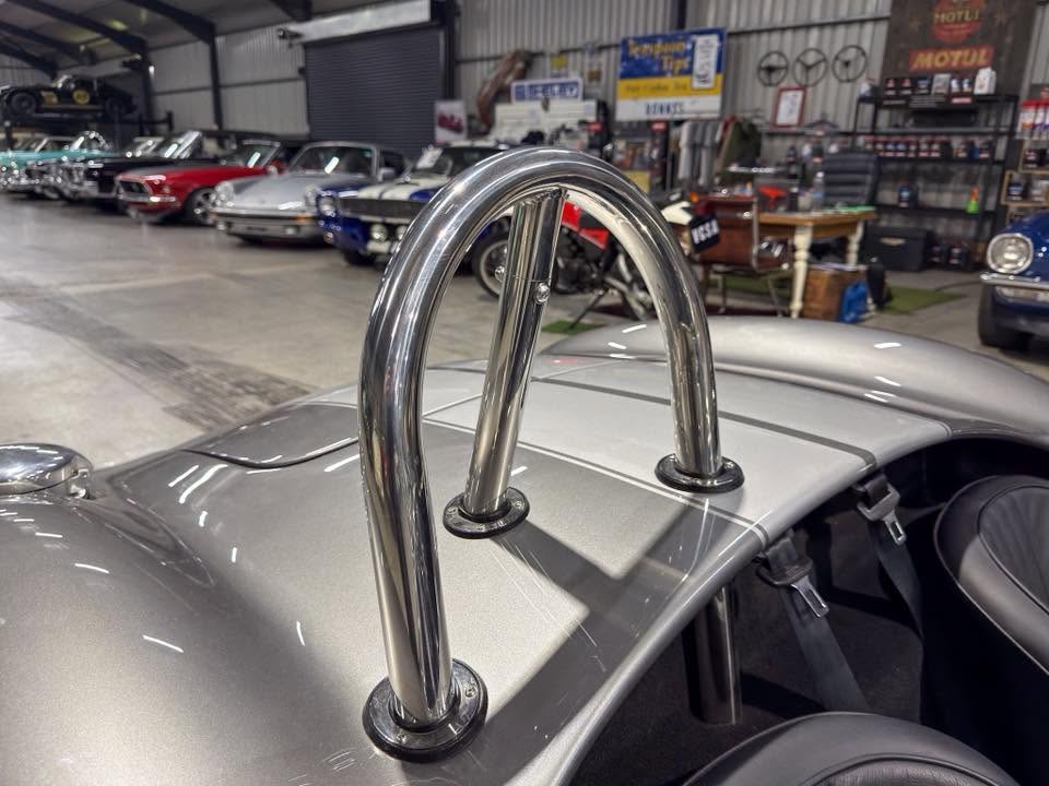 Roll bar on a silver classic sports car inside a garage with other vintage cars and auto memorabilia in the background.