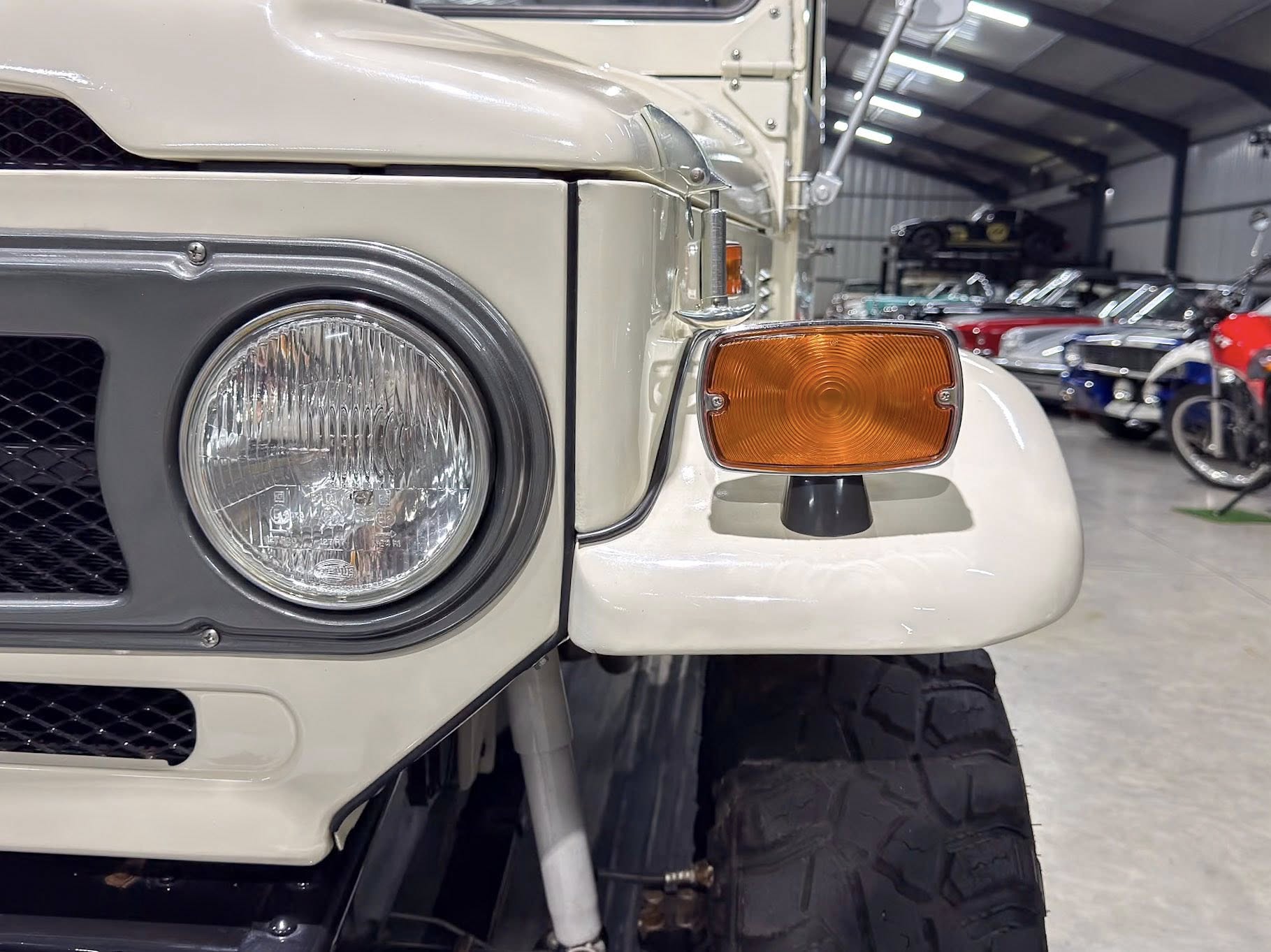 Close-up of a vintage truck's front left corner, showing the round headlight and orange turn signal with a beige body in a car showroom.