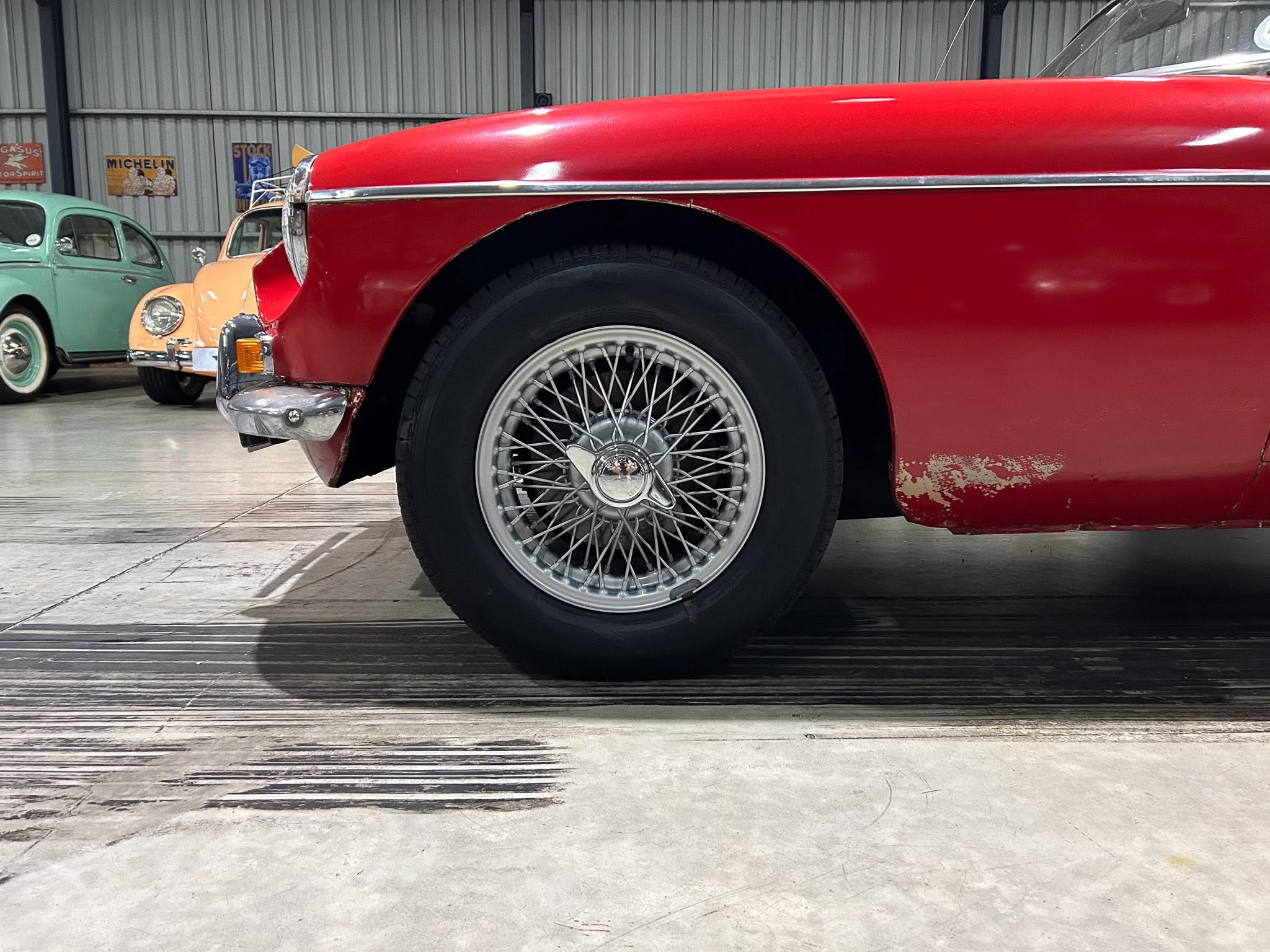 Close-up of a red vintage car front fender and wheel in a showroom with other classic cars in the background.