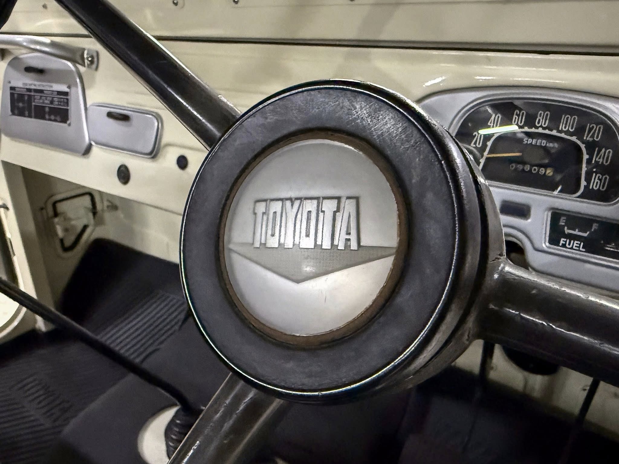 Close-up of a vintage car interior: steering wheel and gauge cluster with a beige dashboard and speedometer up to 160.
