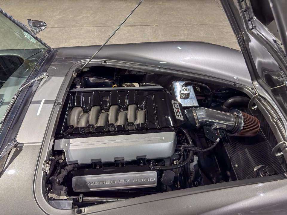 Open car hood reveals a high-performance V8 engine with a prominent 5.0 badge and polished intake manifold.
