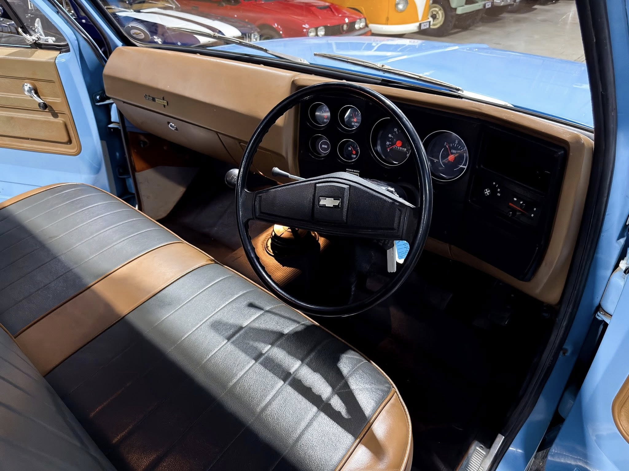 Close-up of a vintage car interior: brown dashboard and black steering wheel with a Chevrolet emblem, tan seats.