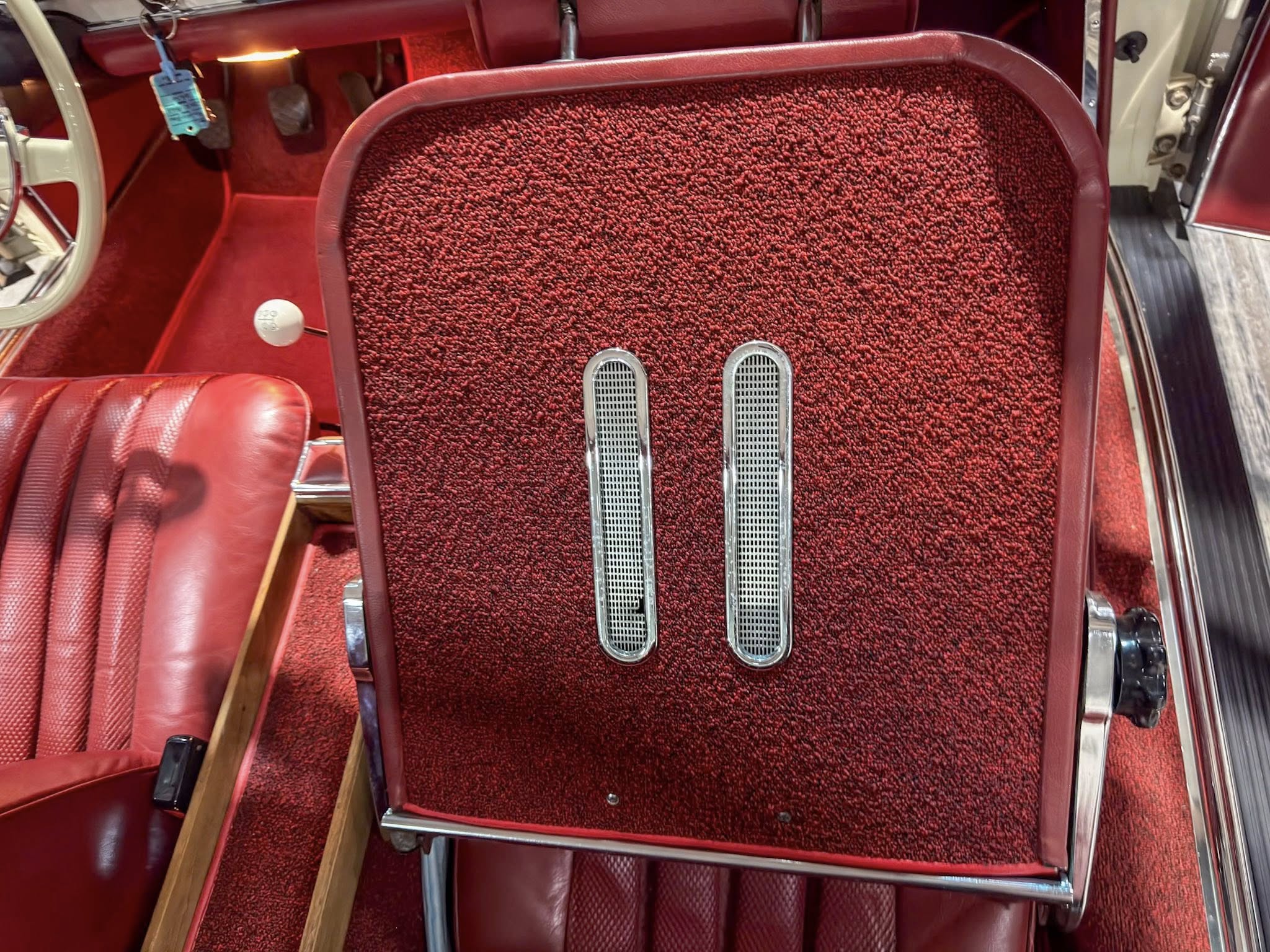 Interior of a vintage red car with red carpet, red leather seats, and two slim chrome pedal covers in the floor?