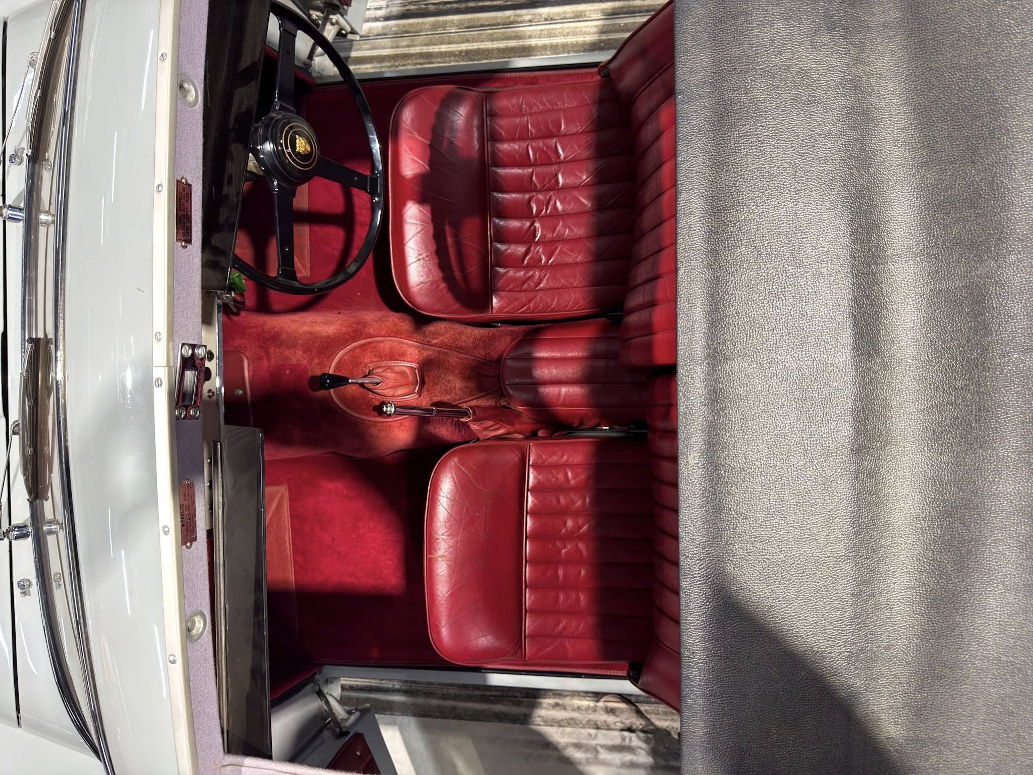Red leather car seats and a black steering wheel inside a vintage car cabin.