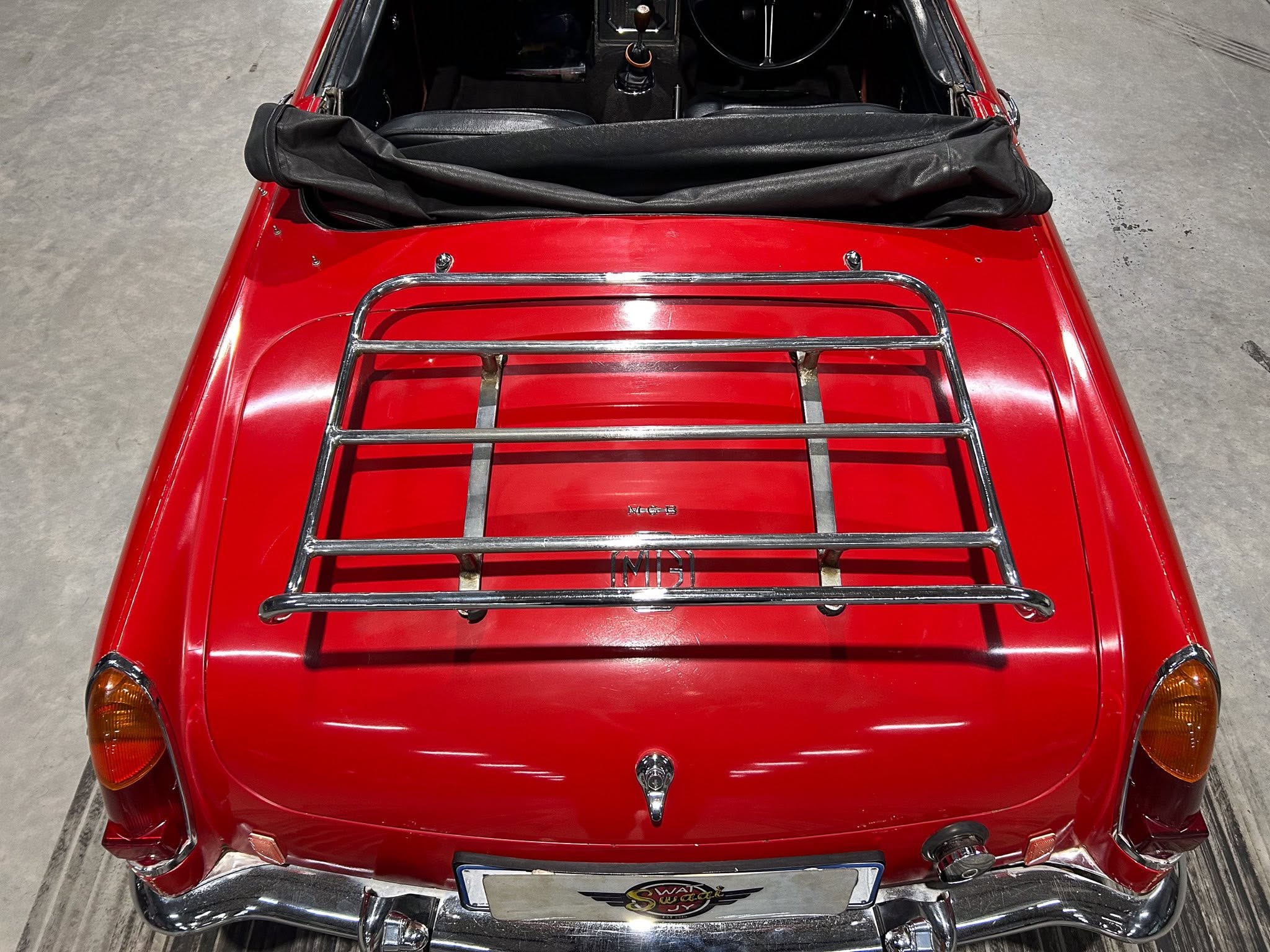 Top-down view of a red vintage convertible with a chrome luggage rack and folded black soft top outside the cabin area