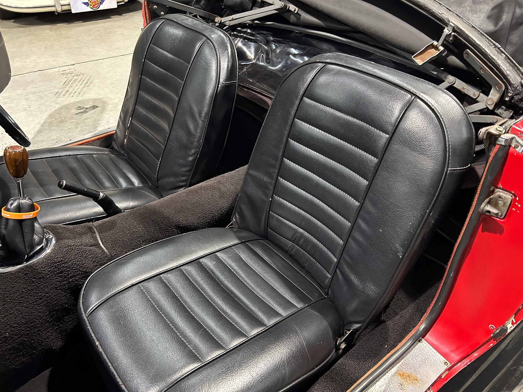 Interior view of a red convertible showing black leather seats with vertical stitching and a wooden gear knob in the foreground.
